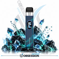 A blue disposable vape device with a digital screen showing 30% battery, standing upright on a reflective surface in front of dark rocks and glowing blue ice crystals. The background is white with Obsession Vape Store branding.