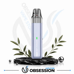 A light lavender vape device with a clear mouthpiece, standing on a black stone slab with decorative green leaves and metallic spheres. The Obsession Vape Store logo is visible at the bottom.