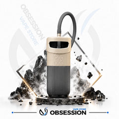 A Obsession OZO vape device in beige and dark gray, displayed with a black mouthpiece, surrounded by stylized black rocks, smoke effects, and geometric gold frames on a white background with Obsession branding.