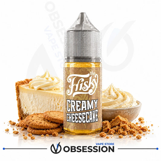 A bottle of Obsession by The Frisky Creamy Cheesecake e-liquid centered on a white background, flanked by a slice of cheesecake, whipped cream, cookies, and cookie crumbs. The bottle label reads 'The Frisky Creamy Cheesecake'.