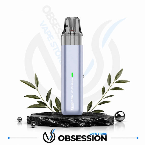 A light lavender vape device with a clear mouthpiece, standing on a black stone slab with decorative green leaves and metallic spheres. The Obsession Vape Store logo is visible at the bottom.