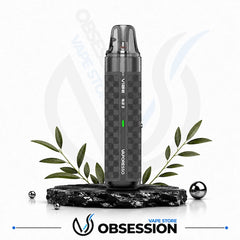 A dark gray Vibe 2 disposable vape device with a checkered pattern, displayed on a black marble base with decorative green leaves and metallic spheres against a white background with a faint store watermark.