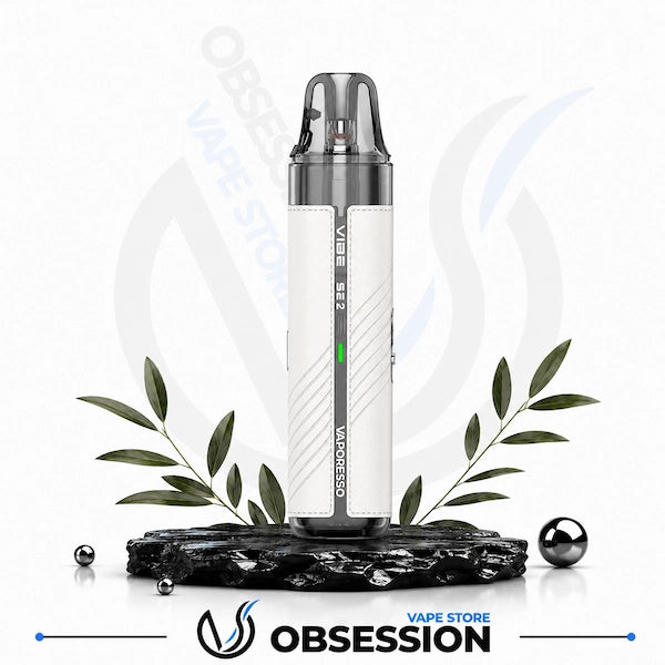 A white and silver Vaporesso XROS vape device displayed on a black marble base with decorative green leaves and small metallic spheres against a white background with a faint Vaporesso logo.