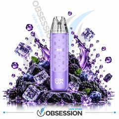 A purple disposable vape device with a clear mouthpiece, centered over a pile of ice cubes, blueberries, and blackberries on a white background. Purple liquid splashes and droplets surround the device.
