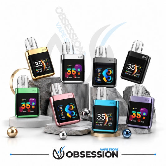Eight small rectangular electronic devices with colorful metallic bodies and black front screens are arranged on gray rocks and pedestals against a white studio background. The devices come in gold, silver, black, green, pink, blue, and purple colorways.