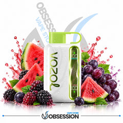 A white Vozol disposable vape device with a bright green mouthpiece and side display, surrounded by fresh watermelon slices, blueberries, and blackberries on a white background with Obsession Vape Store branding.
